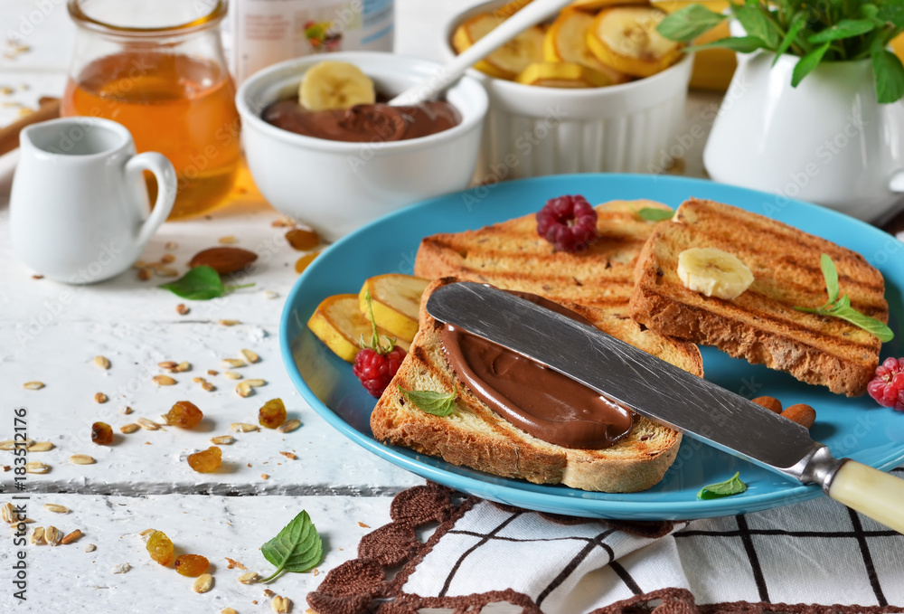 Good morning - toast with walnut, chocolate paste, banana and honey. White food background. Good morning - toast with walnut, chocolate paste, banana and honey. White food background.