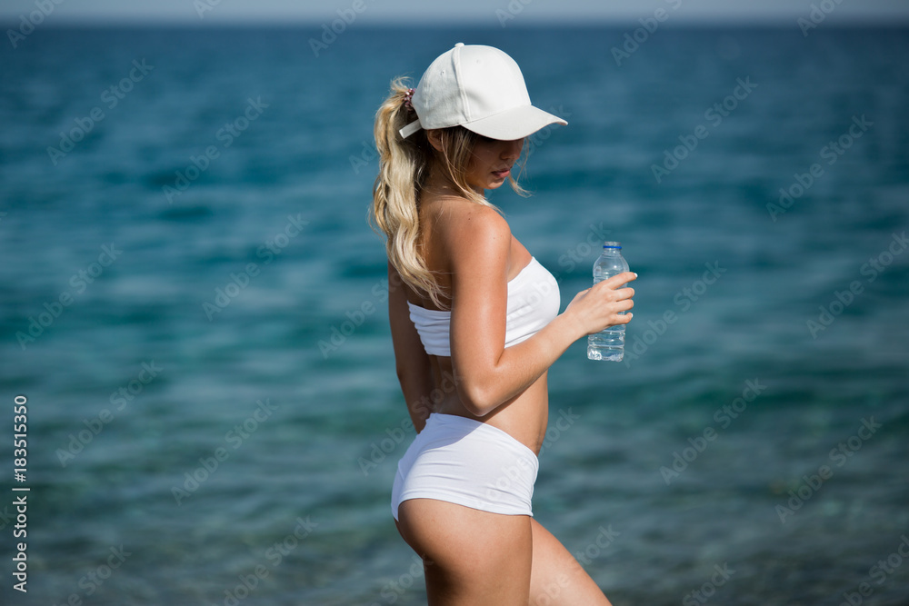 Slim girl in white sportswear with bottle of water standing outdoors on the beach, close up back view Slim girl in white sportswear with bottle of water standing outdoors on the beach, close up back view