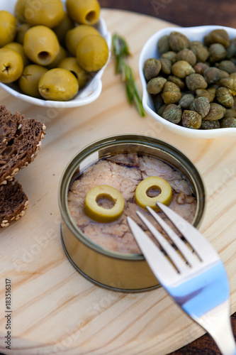 Tuna can next to a bowl of olives and capers