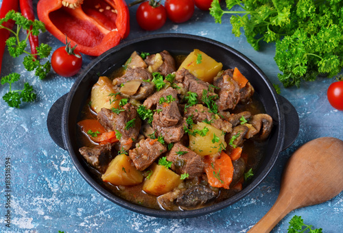 Meat goulash with vegetables, potatoes and mushrooms on concrete, grunge background