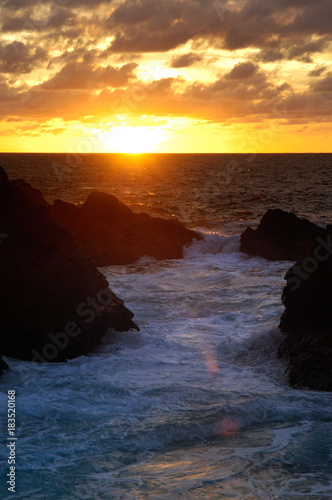 Waves of the Pacific ocean beat against the rocks in sunset light