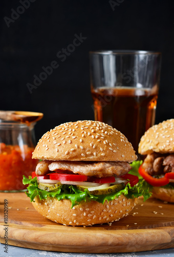 Big homemade burger with meat, tomato and sauce on a cutting board. Concrete background. Fast food.