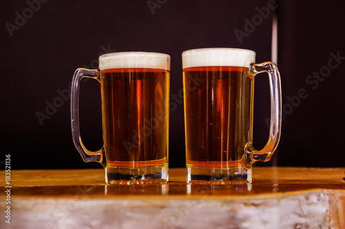 Indoor view of two glasses of beer on a wooden table in a black background