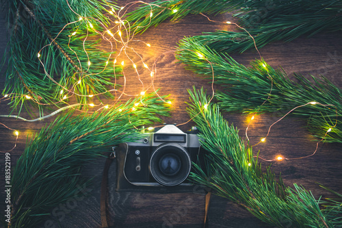 The old camera on a wooden background with Christmas tree branches and lights.