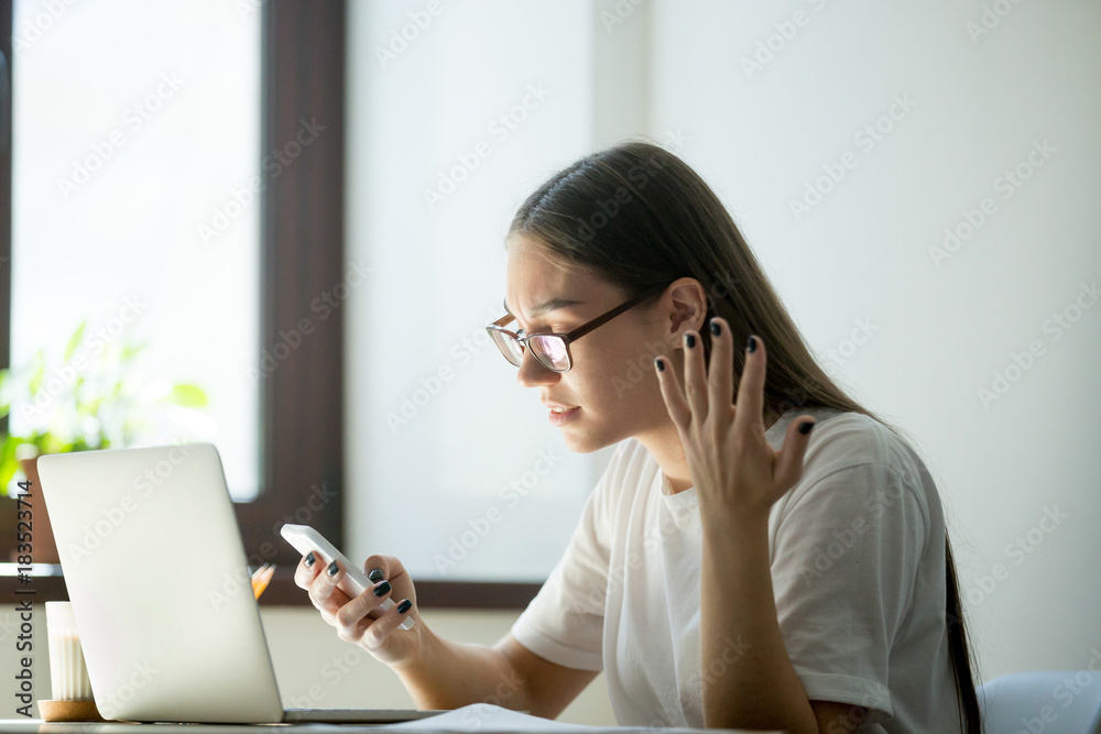 Young furious woman receiving bad negative news, spam in messages on smartphone. Broken mobile cellphone not working and needs charge Young furious woman receiving bad negative news, spam in messages on smartphone. Broken mobile cellphone not working and needs charge