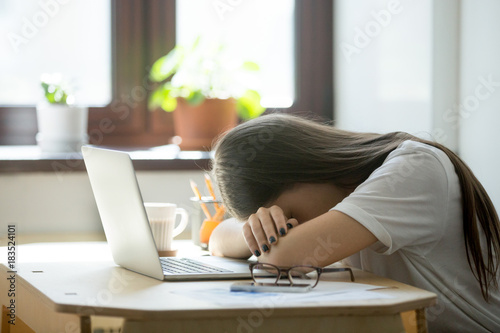 Tired young woman falling asleep at desk after overwork. Exhausted sleep deprived stressed female manager lying on table and sleeping after hard working day, no energy left photo