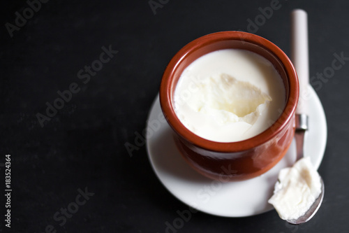 Sour  cream or natural  Cottage cheese curd in clay pot on dark  background. Traditional Cuajada yogurt cream