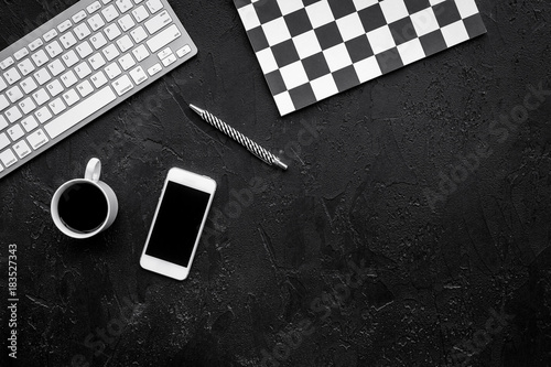 Concept of the strict office desk in monochrome. Keyboard, notebook, cell phone,  coffee on black background top view copyspace