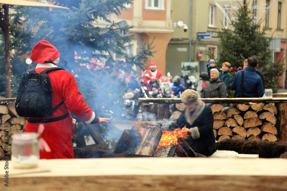 Święty Mikołaj grzeje dłonie przy ognisku na rynku w Opolu. - obrazy, fototapety, plakaty 