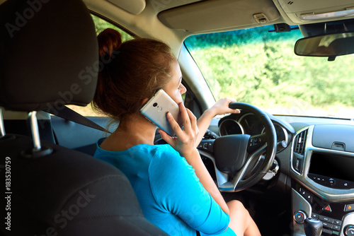 Back view of beautiful young woman driving a car and talking on smart phone, free space. Business woman sitting in car with cell phone,  looking on road © mirage_studio