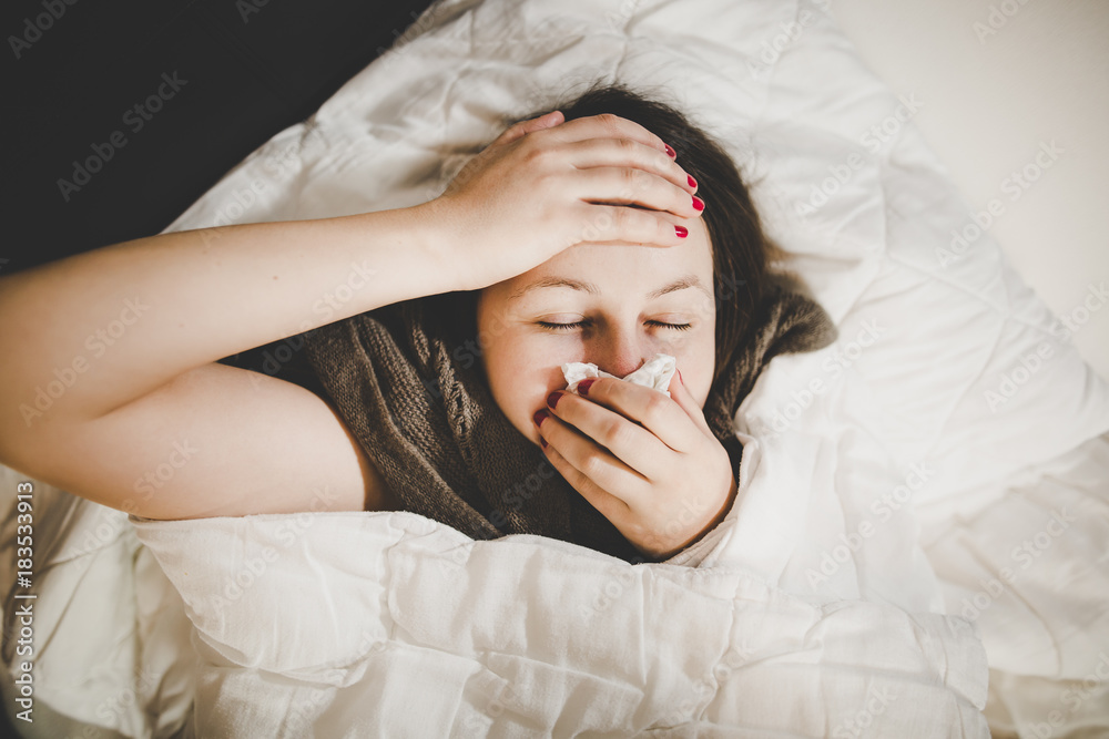 Pretty young brunette woman resting in a bed with cough, looking sick and illness (color toned image)