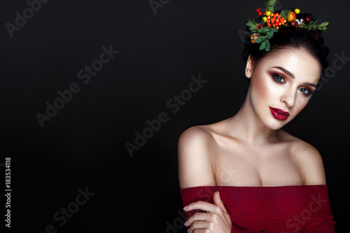 Beautiful woman portrait with red and yellow berries on head and with black hair and red lips.