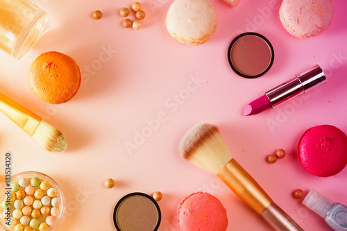 Make up products and macaroons flat lay scene on pink background, toned
