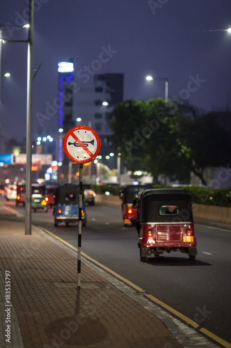 A lot of three-wheeled tuk-tuk and other transport pass by the road sign 