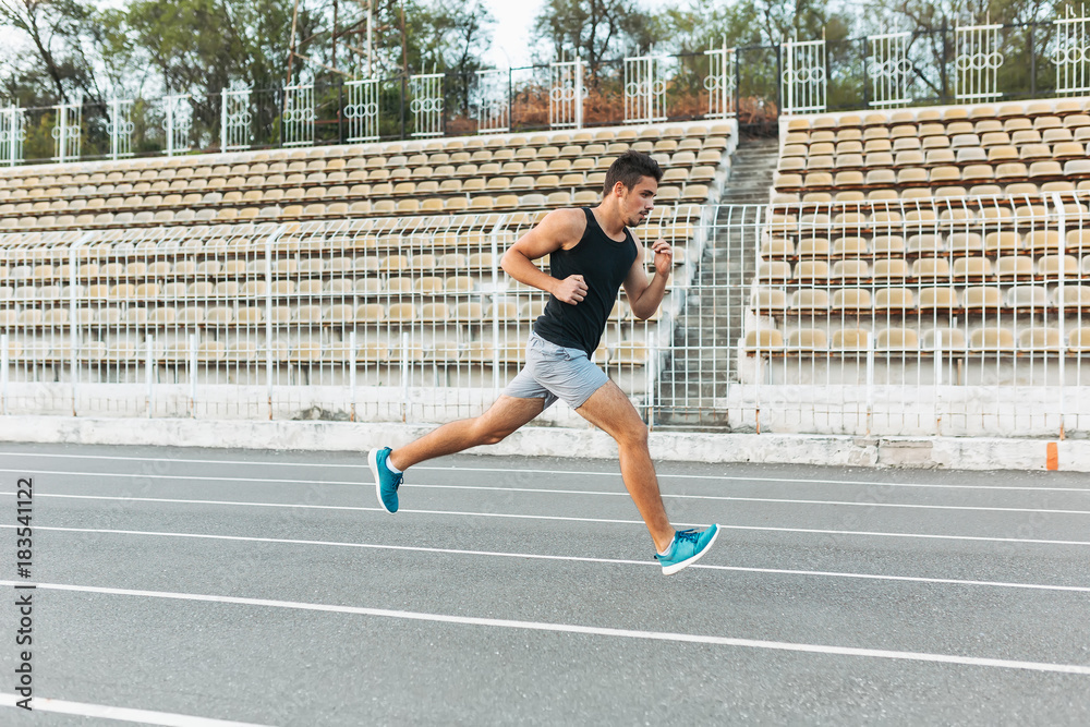 Fototapeta premium Young athletic man running on the stadium in the morning