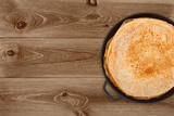 Crepes in a cast iron pan on dark wooden background, top view