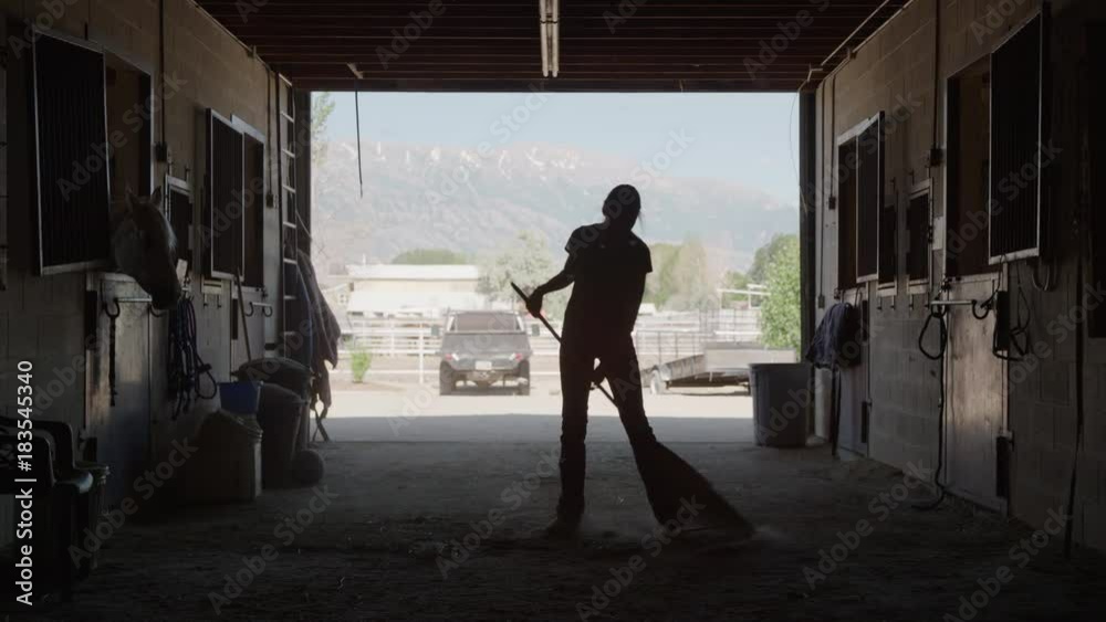 Wide slow motion silhouette of girl cleaning floor of stable / Lehi, Utah, United States