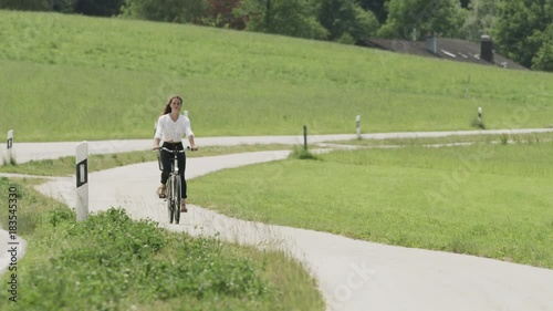 Wide slow motion shot of distant woman approaching on bicycle / Ainring, Bavaria, Germany photo