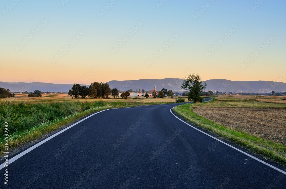 Summer rural landscape. Asphalt road with mountains and village in the background.