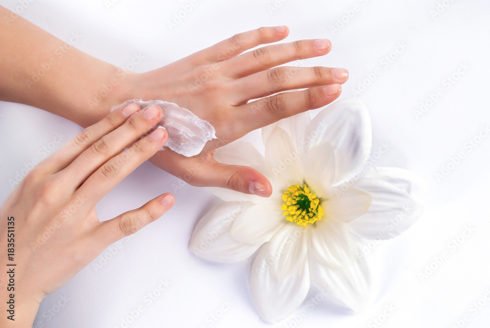 Young woman applying cream on beautiful and manicured hands and white flower in background