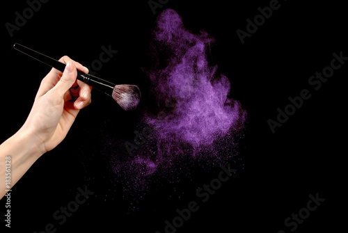 Woman hand holding make up brush with powder dust isolated on black background