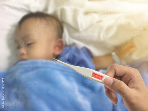 Hand holding digital thermometer with high fever over blurry illness asian kid