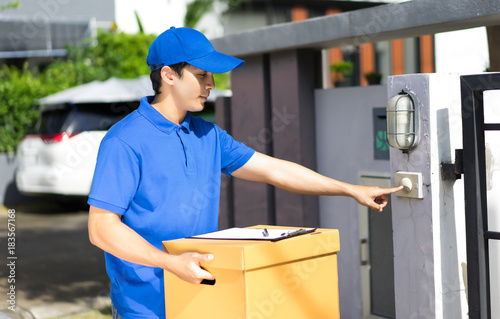 Fotografija Delivery concept - Happy delivery person in blue uniform holding cardboard box s