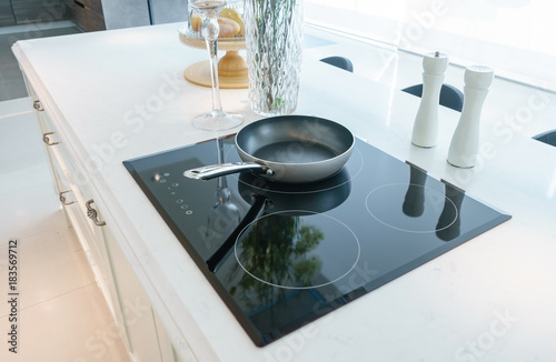Frying pan on modern black induction stove, cooker, hob or built in cooktop with ceramic top in white kitchen interior photo