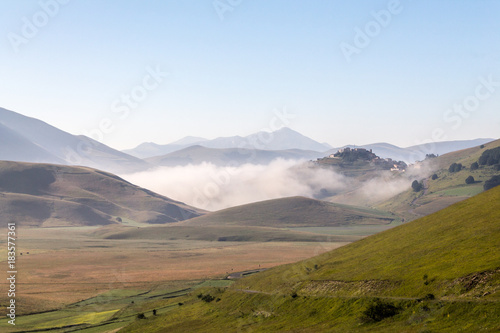 View of Castelluccio di Norcia  Umbria  at dawn  with mist  big meadows and totally empty blue sky