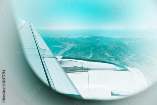 Air traveling and transportation concept. Selective focused on the airplane wing and having blurry mountian in background. Color aquas toned.