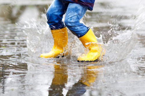 фотографія Close-up of kid wearing yellow rain boots and walking during sleet, rain and sno