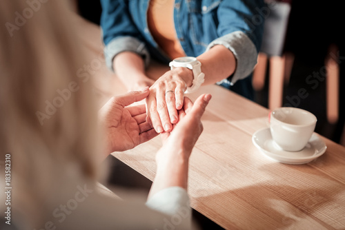 How beautiful. Amazing expensive engagement ring being on the finger of a young lovely woman while her elderly relative looking at it and a cup of coffee standing on the table not far from their hands