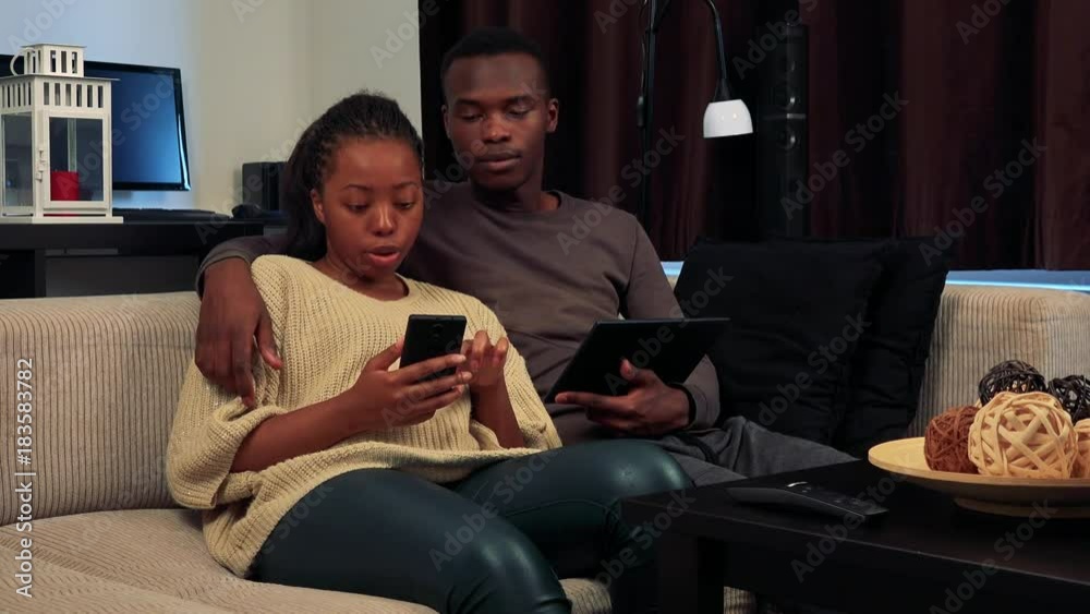 Young black couple work on smartphone and tablet in living room Young black couple work on smartphone and tablet in living room