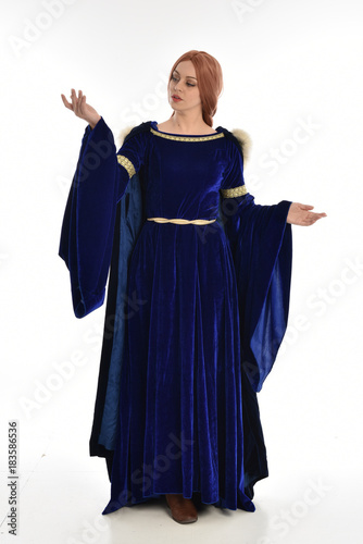 full length portrait of girl wearing long blue velvet gown and fur lined cloak, standing pose on white background.