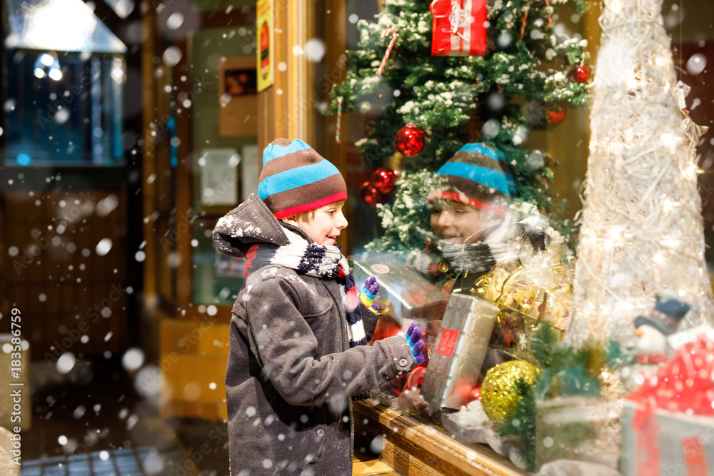 Funny happy child in fashion winter clothes making window shopping decorated with gifts, xmas tree Funny happy child in fashion winter clothes making window shopping decorated with gifts, xmas tree