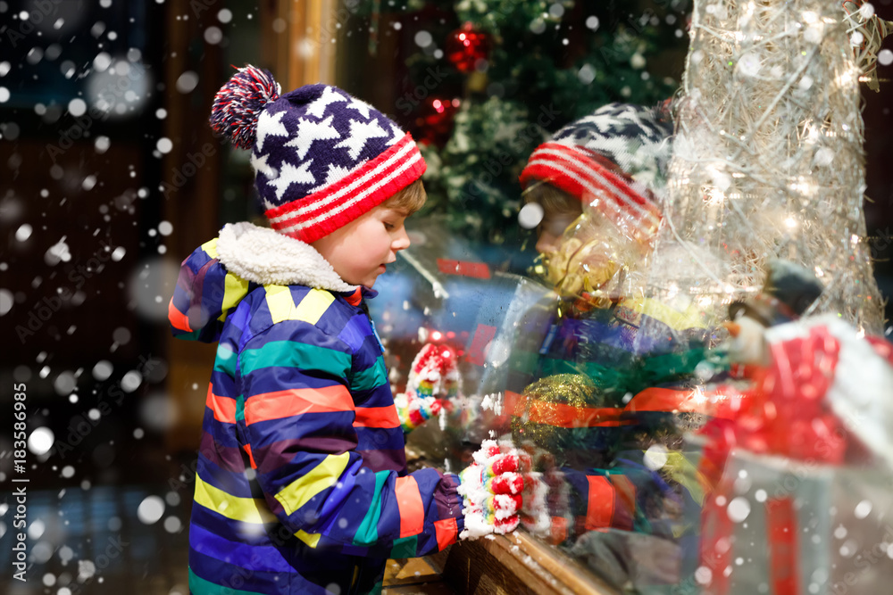Funny happy child in fashion winter clothes making window shopping decorated with gifts, xmas tree Funny happy child in fashion winter clothes making window shopping decorated with gifts, xmas tree