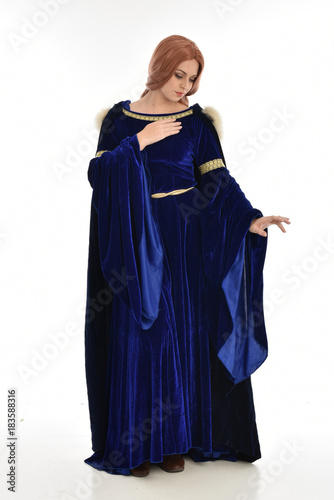 full length portrait of girl wearing long blue velvet gown and fur lined cloak, standing pose on white background.
