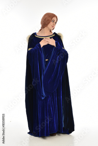 full length portrait of girl wearing long blue velvet gown and fur lined cloak, standing pose  on white background.