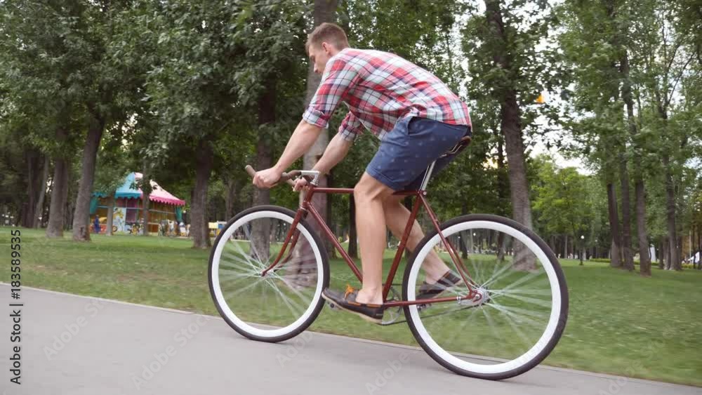 Sporty guy cycling at the park road. Young handsome man riding a vintage bicycle outdoor. Healthy active lifestyle. Side view Close up Slow motion Sporty guy cycling at the park road. Young handsome man riding a vintage bicycle outdoor. Healthy active lifestyle. Side view Close up Slow motion