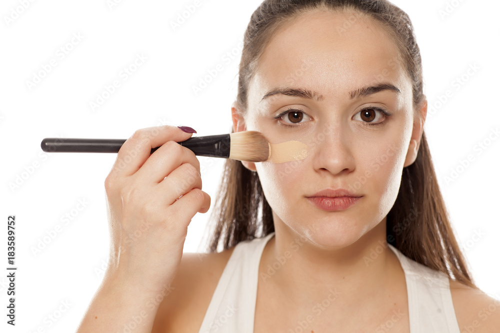 young woman applying a liquid foundation on her face with a brush young woman applying a liquid foundation on her face with a brush
