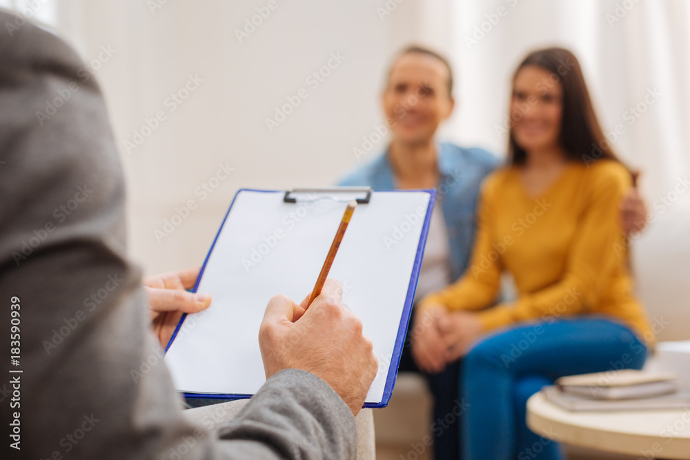 Worth to remember. Selective focus of male psychologist hands which holding blue folder and yellow pencil on the blurred background during session Worth to remember. Selective focus of male psychologist hands which holding blue folder and yellow pencil on the blurred background during session