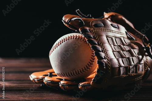 Photography close-up view of white leather baseball ball and glove on wooden table