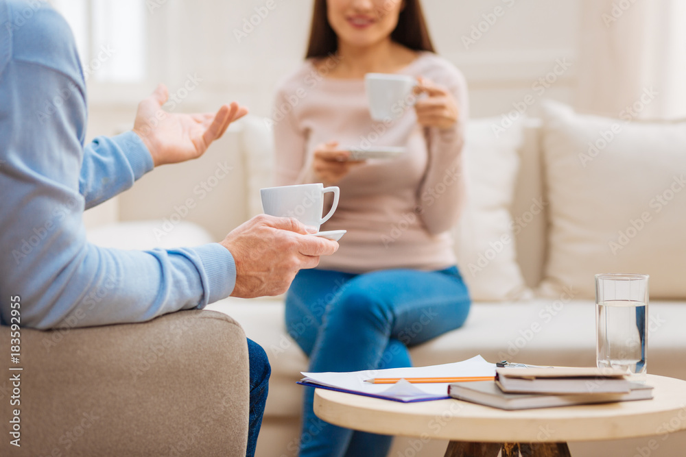 Coffee time. Selective focus of coffee table where folder books water lying and hand which carrying cup during pleasant conversation Coffee time. Selective focus of coffee table where folder books water lying and hand which carrying cup during pleasant conversation