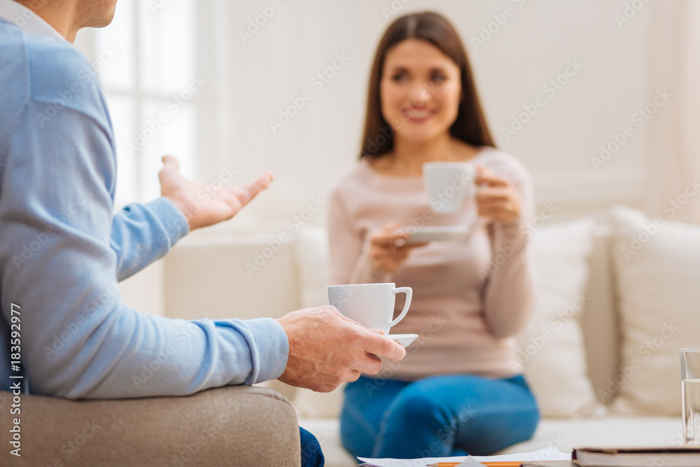 Pleasure from tea. Selective focus of tea cup hold by male young hand with positive optimistic woman drinking tea on the background Pleasure from tea. Selective focus of tea cup hold by male young hand with positive optimistic woman drinking tea on the background