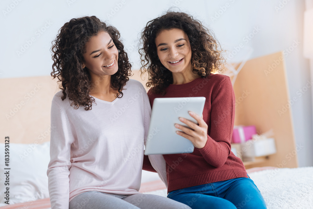 Favorite leisure activity. Selective focus on two radiant girls in casual grinning broadly while embracing and using a tablet computer together. Favorite leisure activity. Selective focus on two radiant girls in casual grinning broadly while embracing and using a tablet computer together.