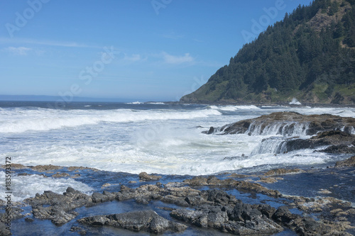 Beach on the Oregon Coast with waves, white water, mountain, rocks and tide pools against a blue sky