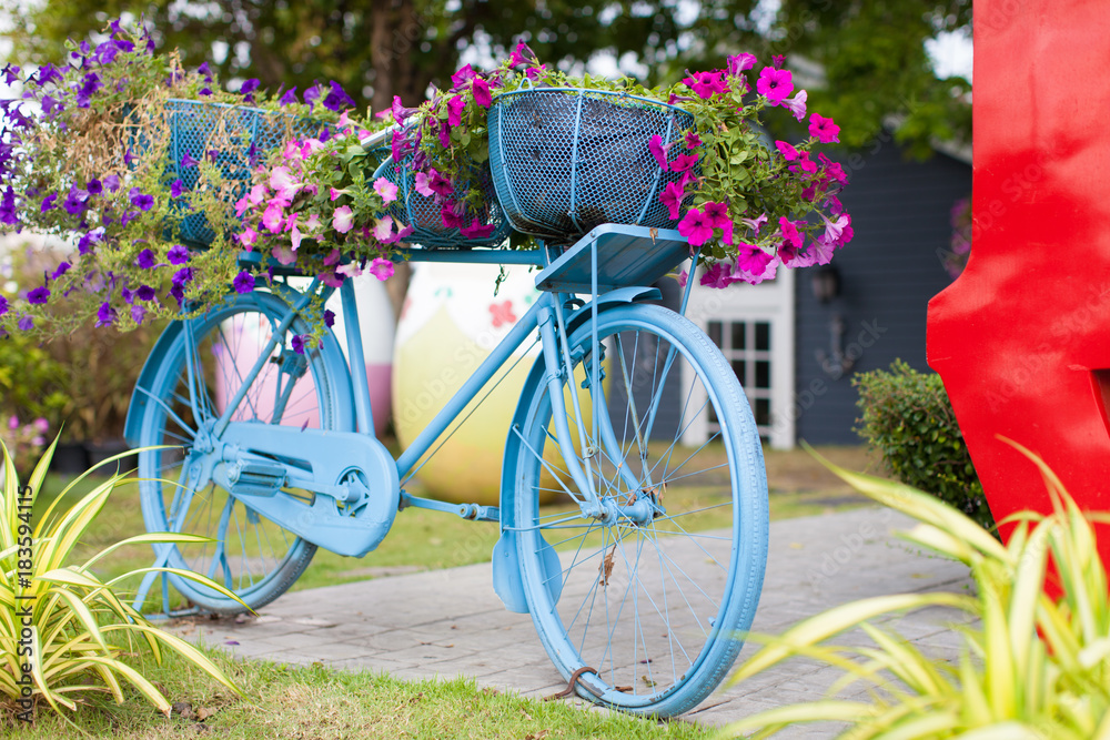 Blue bicycle with flowers stand in a garden.
