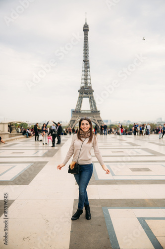 Beautiful girl posing to the photographer against the background of the Eiffel Tower. Autumn photosession. Sunny weather. Beautiful smile and makeup © Aleksandr