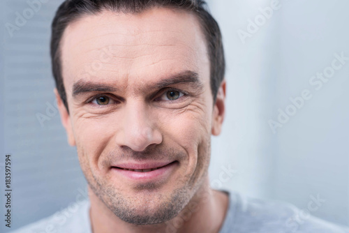 Kind smile. Close up of attractive cute cheerful man posing on light background while looking straight and enjoying life 