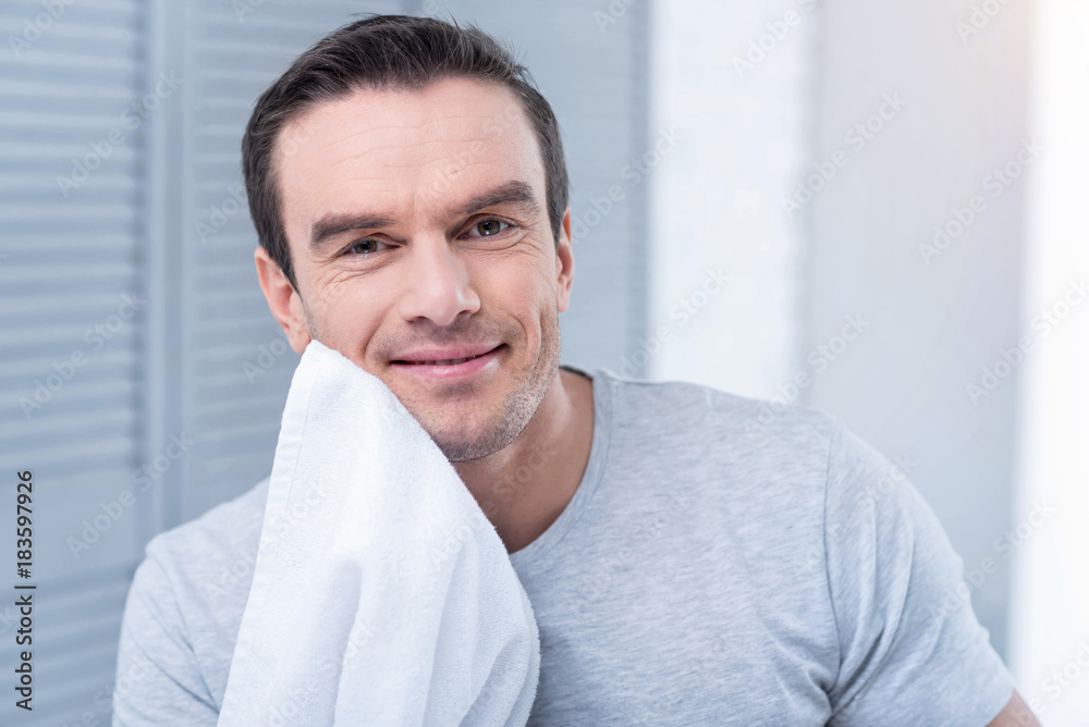 Good morning. Pleasant energetic cheerful man scratching his chick with a towel and grinning while wearing grey shirt Good morning. Pleasant energetic cheerful man scratching his chick with a towel and grinning while wearing grey shirt